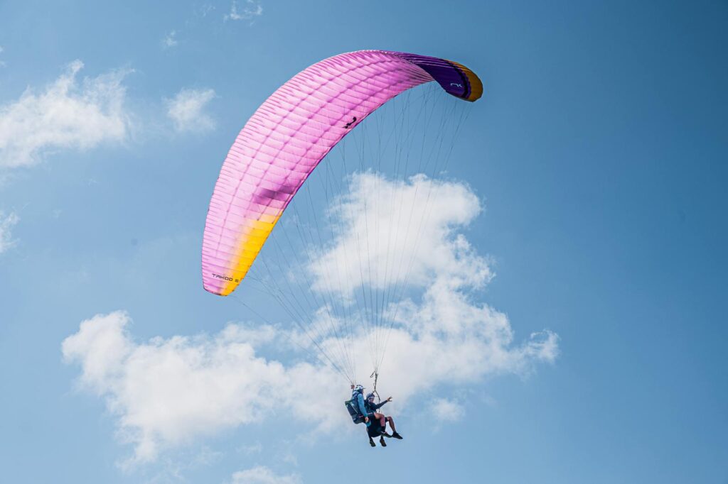 Experience the thrill of tandem paragliding with colorful parachute soaring high in the clear blue sky.