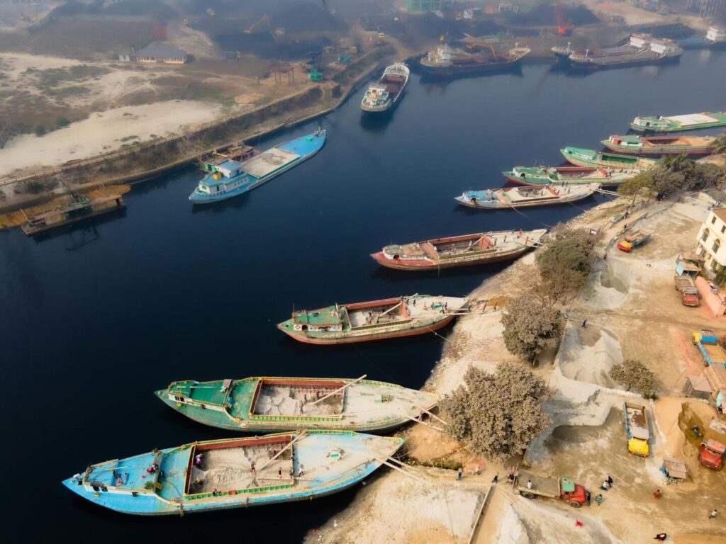 Aerial image of cargo ships docked at a river port with industrial and natural landscapes.