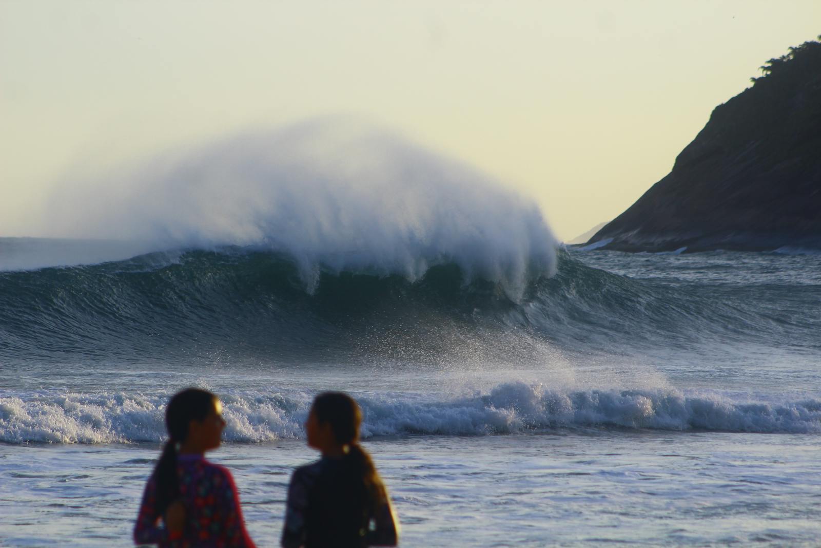 Silhouetted people watch huge waves crash on a Rio de Janeiro beach at sunset.