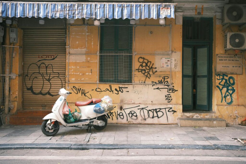 A classic scooter parked by a graffiti-covered wall in Hanoi, Vietnam, showcasing urban street art and culture.