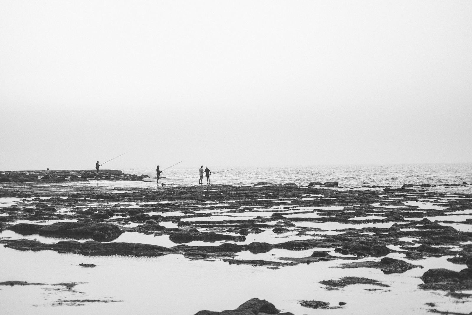Black and white photo of people fishing on the rocky coast of Rabat, Morocco.