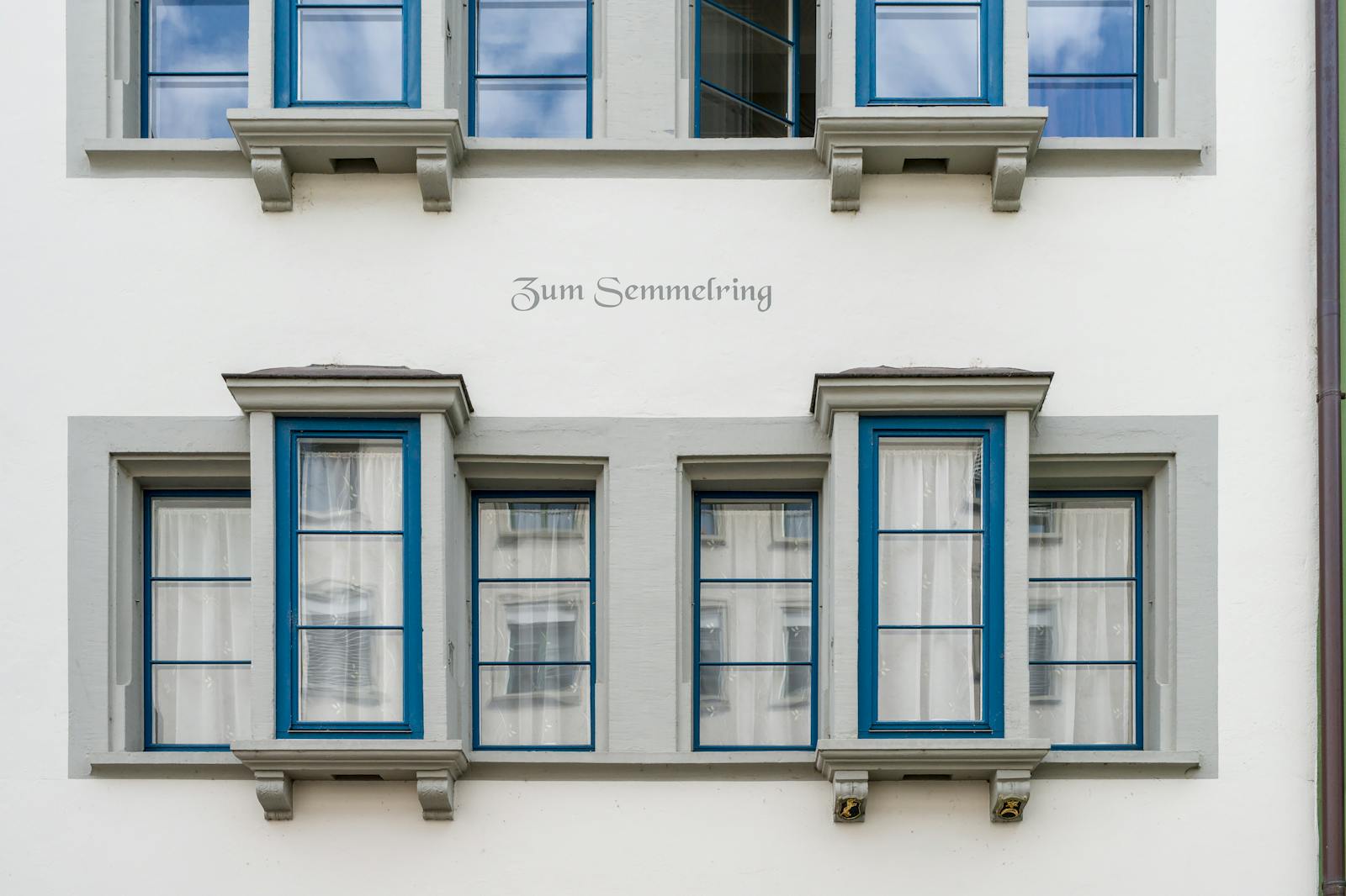 Detail of traditional Swiss architecture with distinctive blue-framed windows and decorative text.