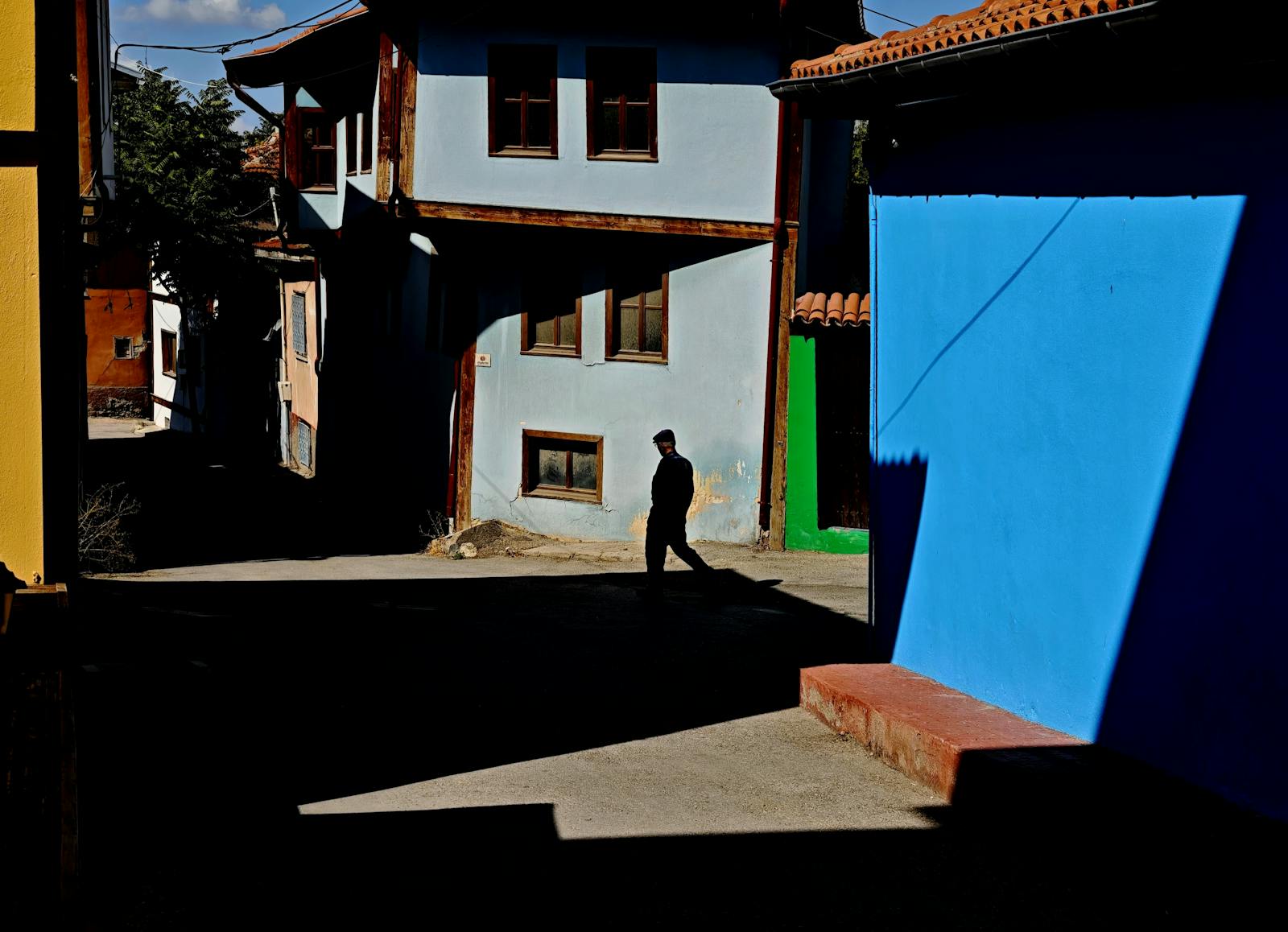 A silhouette of a person walking in Eskişehir with vibrant blue and yellow building facades casting dramatic shadows.